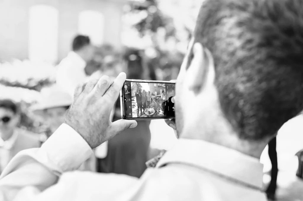 Le photographe de mariage à Toulouse prend en photo un invité qui est entrain de prendre une photo des mariés avec son téléphone