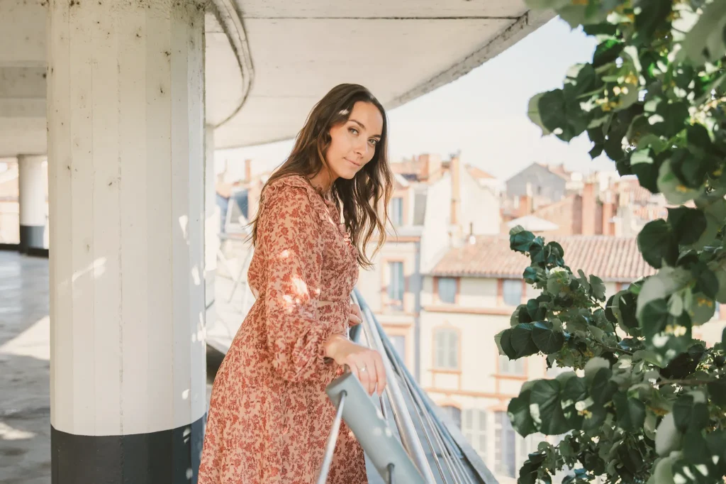Séance portrait à Toulouse dans le parking des Carmes avec Claire. Dans le parking en colimaçon des Carmes, Claire, les mains sur le garde-fou, regarde la ville rose. En face d'elle un tilleul apporte un peu de verdure à ce paysage urbain.