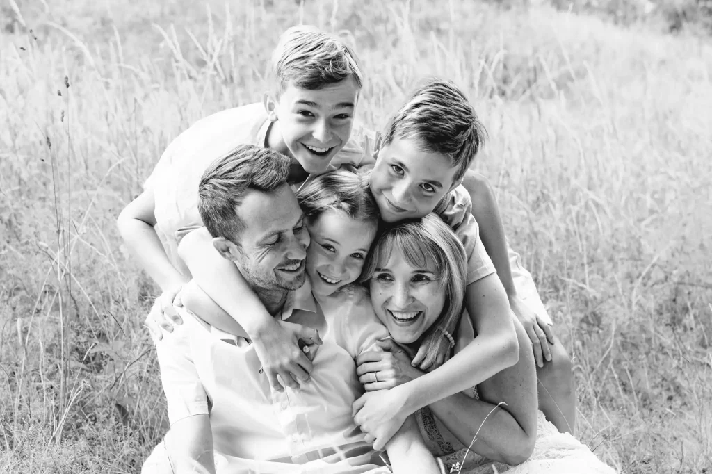Séance photo famille à Toulouse dans la forêt de Bouconne. La famille, assise dans l'herbe, se prend dans les bras.