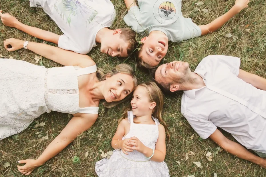 Séance photo famille à Toulouse dans la forêt de Bouconne avec une famille de cinq. Allongés en cercle dans l'herbe, ils se regardent en souriant.