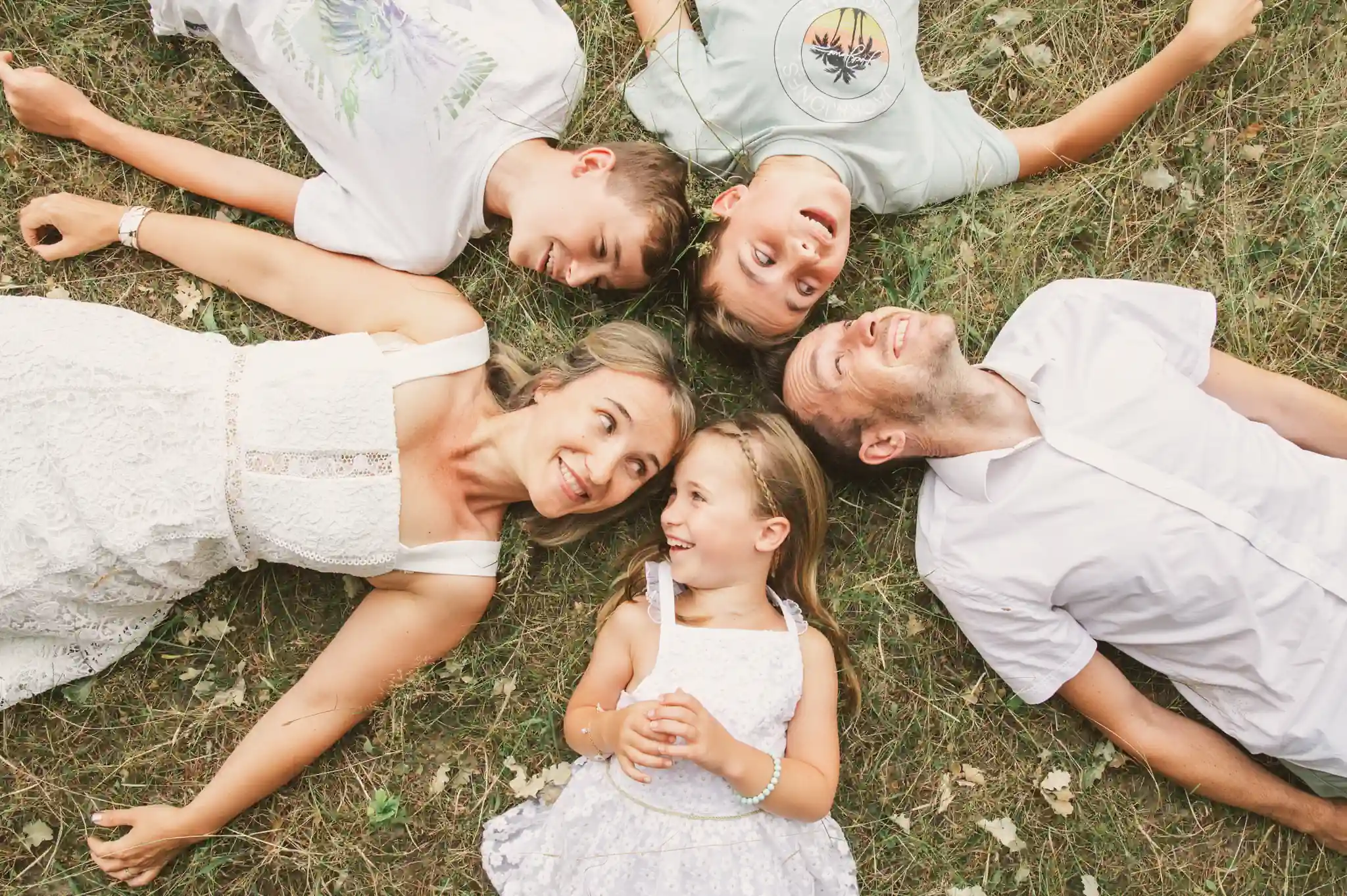 Séance photo famille à Toulouse dans la forêt de Bouconne avec une famille de cinq. Allongés en cercle dans l'herbe, ils se regardent en souriant.