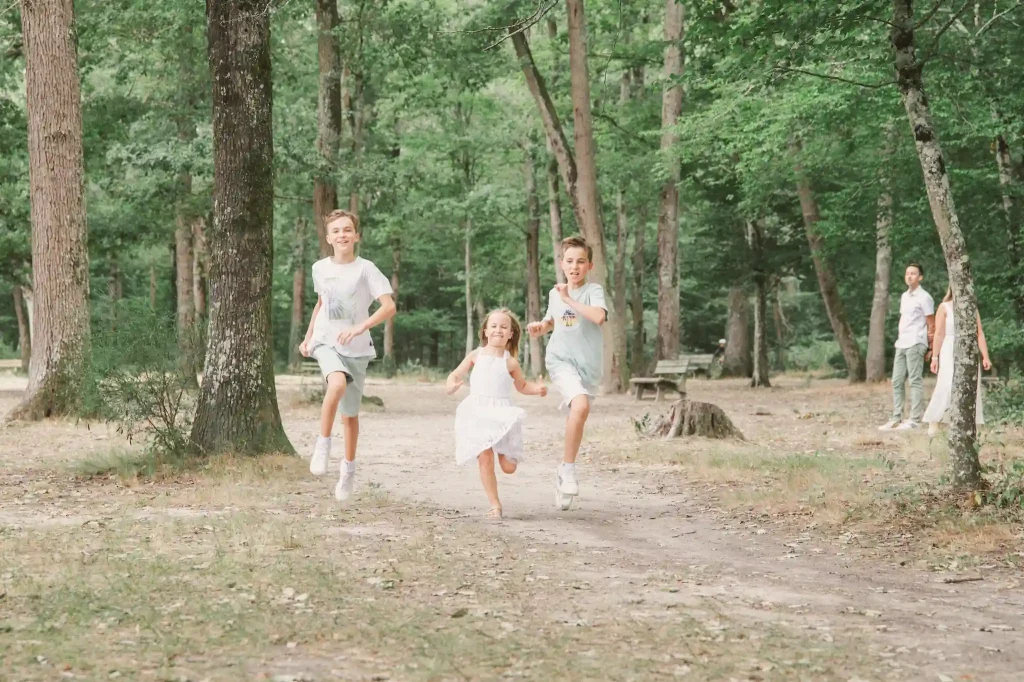 Séance photo famille à Toulouse avec des enfants plein d'énergie. Les enfants courent au milieu des arbres de la Forêt de Bouconne.
