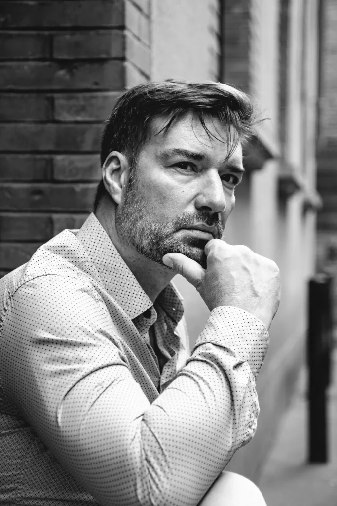 Séance photo portrait à Toulouse dans le quartier des Carmes avec Patrick. Assis sur les marches menant à un immeuble, Patrick regarde au loin, songeur, la main contre le menton.