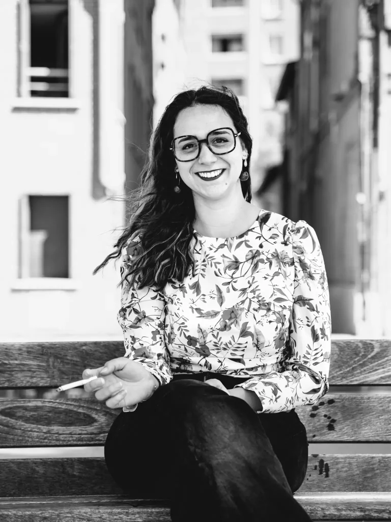 Une séance photo portrait à Toulouse sur les bords de Garonne avec Léa. Elle est assise sur un banc, face à la Garonne et fume une cigarette. Elle nous regarde en souriant.