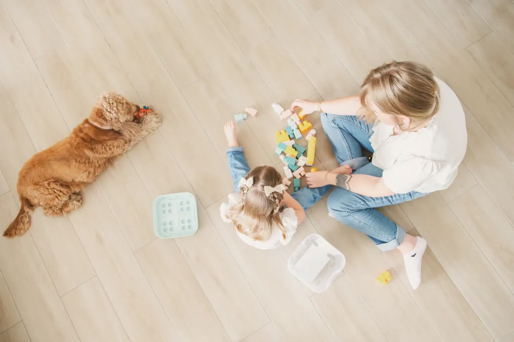 Séance famille à Toulouse. La mère et la fille joue à coté de leur chien qui mâchouille son jouet.
