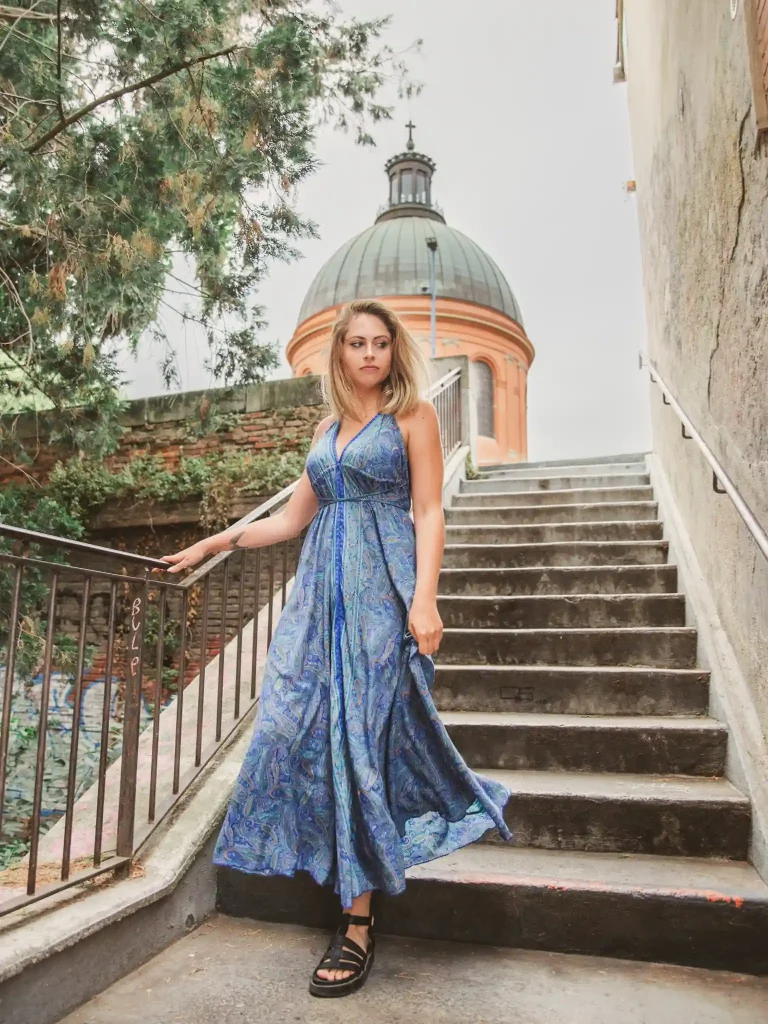 Séance portrait à Toulouse avec vue sur le Dôme de la chapelle Saint Joseph de La Grave. Tina descend les marches menant au pont Saint-Pierre avec sa robe bleue qui vole au vent. En arrière plan le dôme de La Grave fend le ciel.