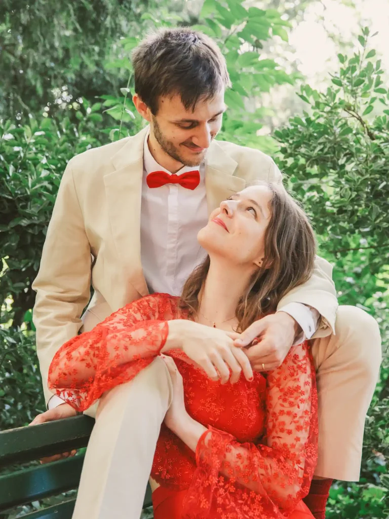Photographe de mariage à Toulouse pour la Day After d'Auriane et Victor qui profite d'un moment de calme, assis sur un banc à se regarder dans les yeux. Victor assis sur le dossier et Auriane entre ses jambes.