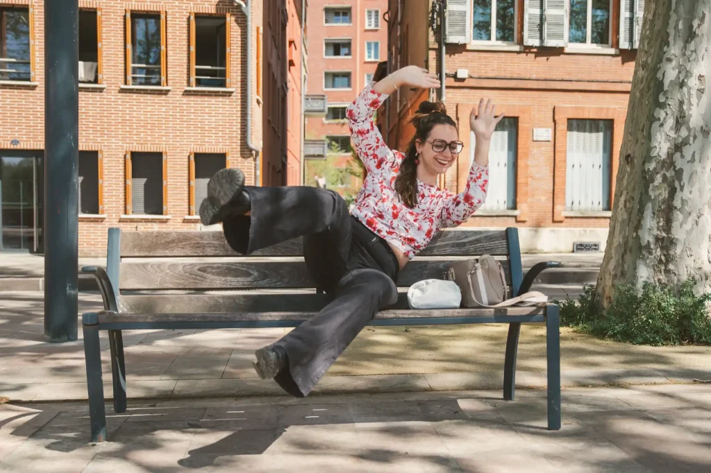 Séance photo portrait à Toulouse sur les bords de Garonne avec Léa. Assise sur le banc elle plaisante et lève les deux bras et deux jambes en l'air