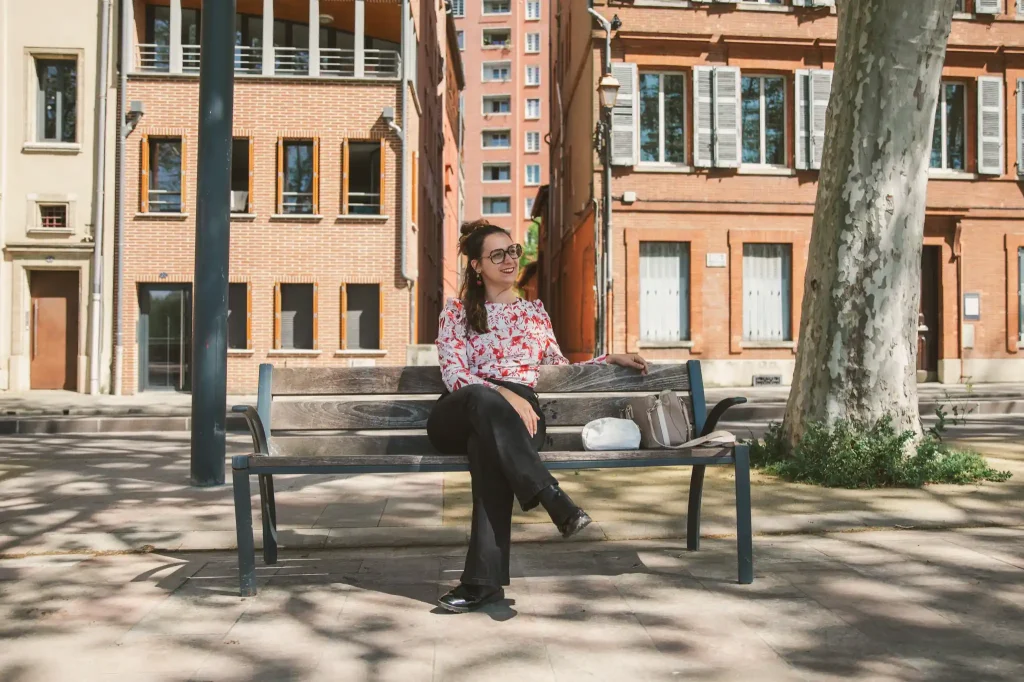 Séance photo portrait à Toulouse sur les bords de Garonne avec Léa qui fait une pose cigarette lors de la séance photo. Assise au milieu du banc, jambes croisées, elle regarde au loin