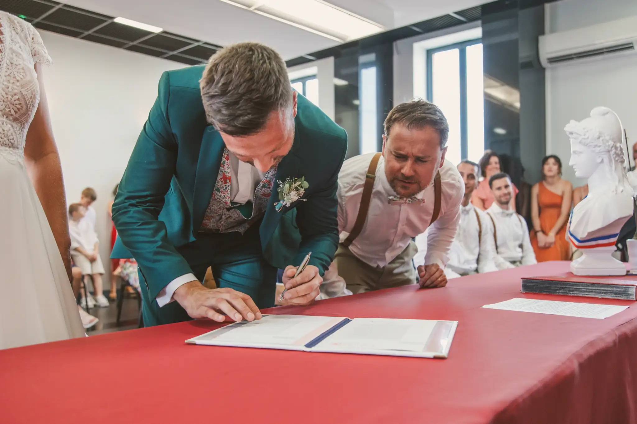 Photographe de mariage à Toulouse lors de la signature du marié à la mairie sous le regard attentif de son témoin.