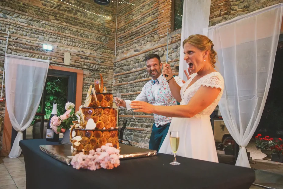 Photographe de mariage à Toulouse, au domaine de Courrèges, la mariée coupe le gâteau en brandissant son couteau.