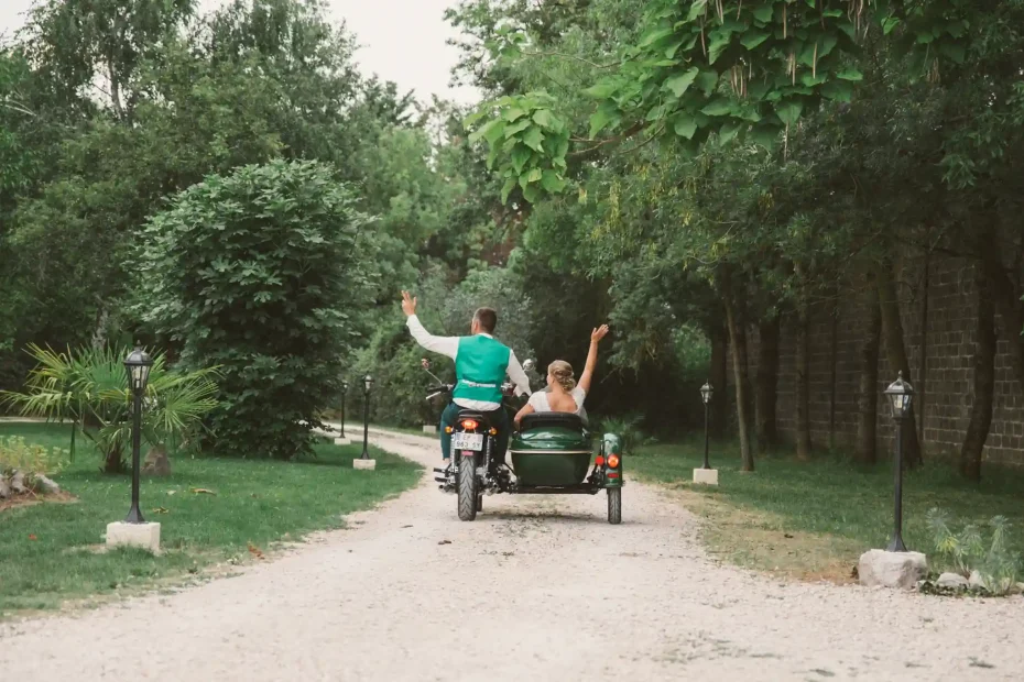 Photographe de mariage à Toulouse, au domaine de Courrèges. Les mariés quittent la réception en side-car. Le marié sur la moto et sa femme à coté font signe de la main en s'éloignant.