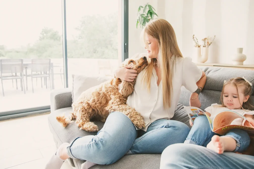 Séance photo famille à Toulouse, sur leur canapé, la maman fait un câlin à son chien.
