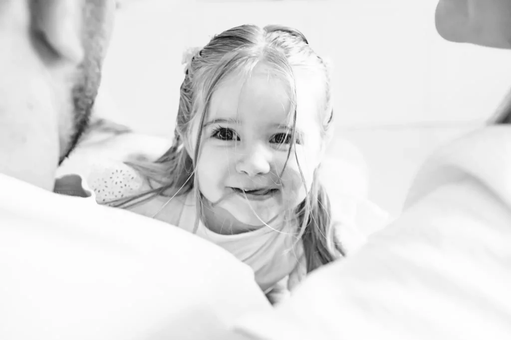Séance photo famille à Toulouse, l'enfant, dans les bras de ses parents nous regarde avec un regard amusé.