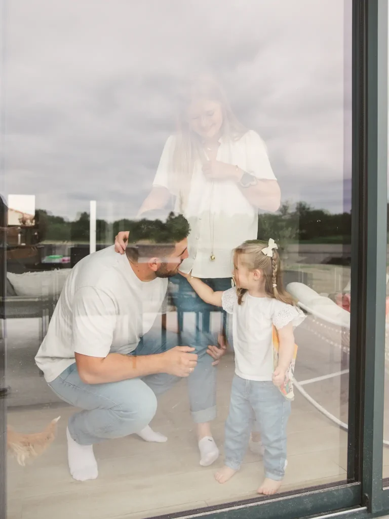 Séance photo famille à Toulouse avec une famille qui s'enlace devant la baie vitrée