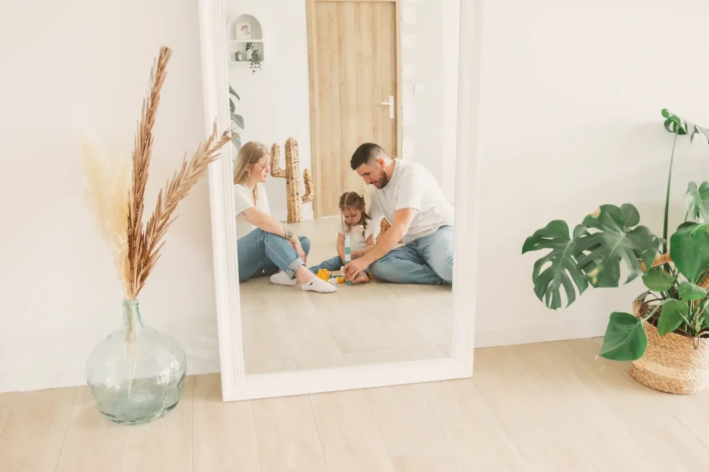Séance photo famille à Toulouse, les parents et leur fille jouent sur le sol du salon, face au miroir.
