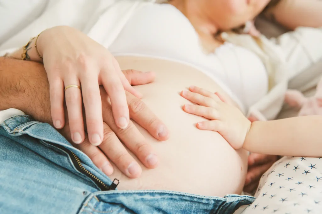 Séance photo grossesse à Toulouse. Allongés sur le lit, toute la famille met sa main sur le ventre de la future maman
