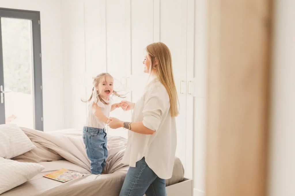 Séance photo grossesse à Toulouse avec la mère et sa fille qui sautent à pieds joints sur le lit en riant