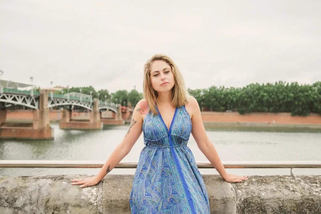 Séance photo portrait à Toulouse sur la digue dans le quartier Saint-Cyprien. Adossée contre la digue, la modèle pose devant la Garonne et le pont Saint-Pierre