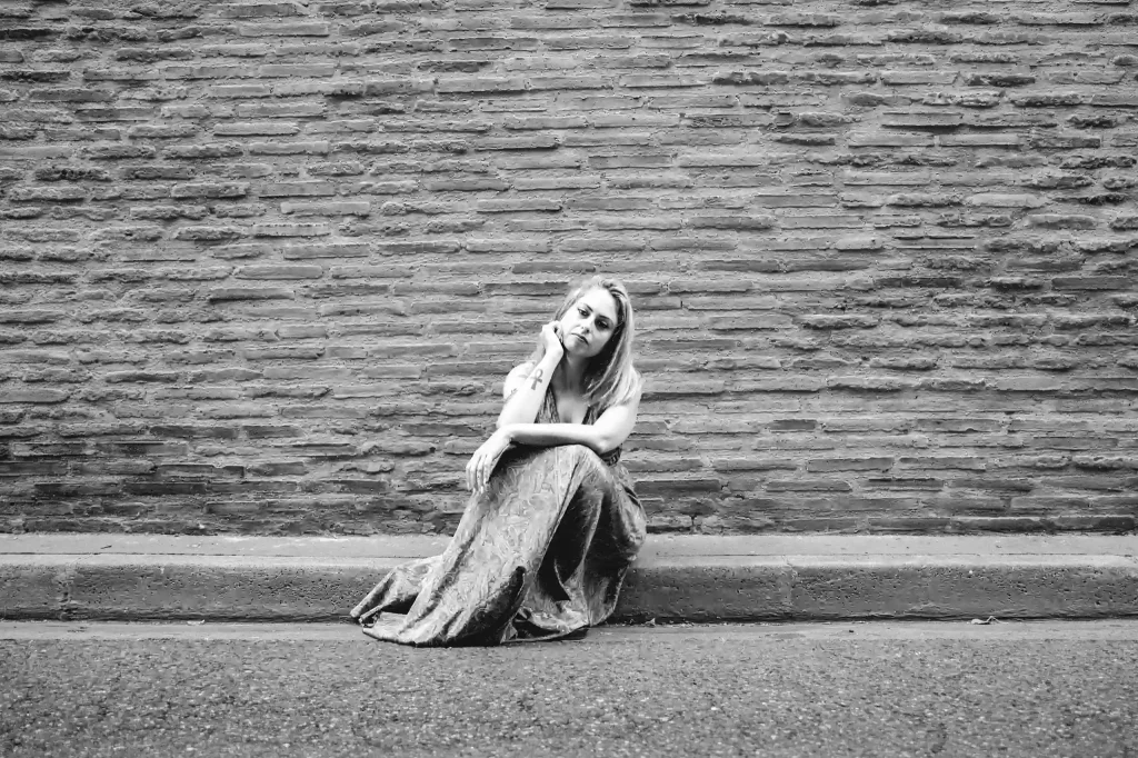 Séance photo portrait à Toulouse dans le quartier Saint Cyprien. Tina assise devant un mur en briques nous regarde.