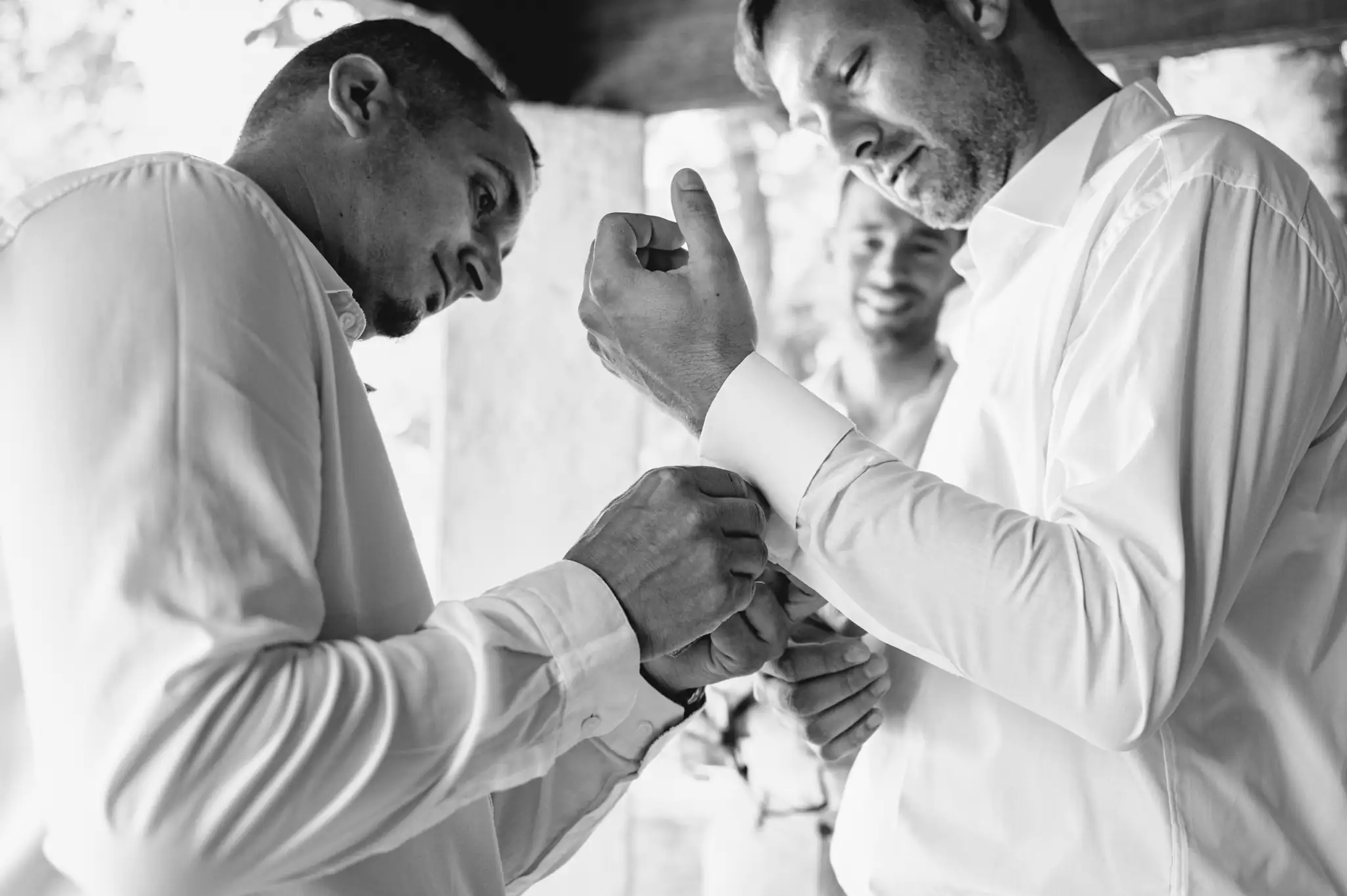 Photographe de mariage à Toulouse, au domaine de Courrèges pendant les préparatifs du marié. Le témoins aide le marié à mettre ses boutons de manchette.