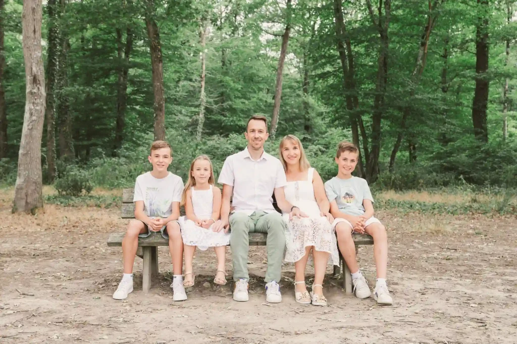 Séance Photo Famille à Toulouse dans la forêt de Bouconne avec une photo de famille assise sur un banc.