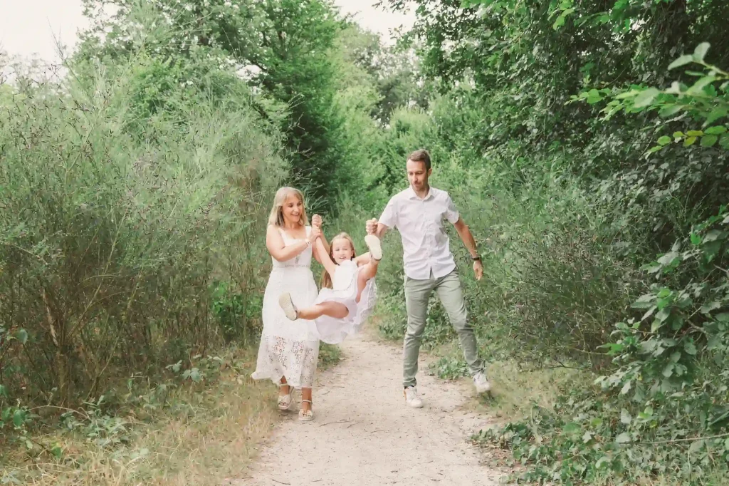 Séance photo famille à Toulouse dans la forêt de Bouconne avec une fille qui se balance sur les bras de ses parents