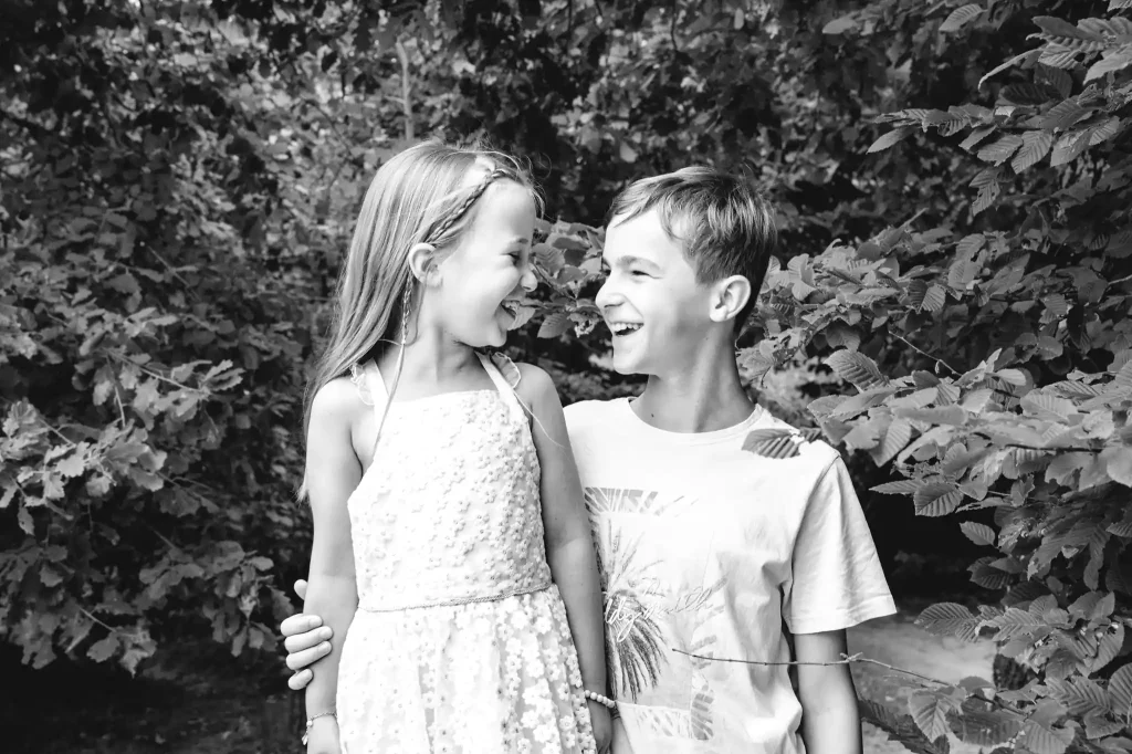 Séance photo famille à Toulouse dans la forêt de Bouconne. Le frère et sa sœur posent cote à cote en se regardant en souriant.
