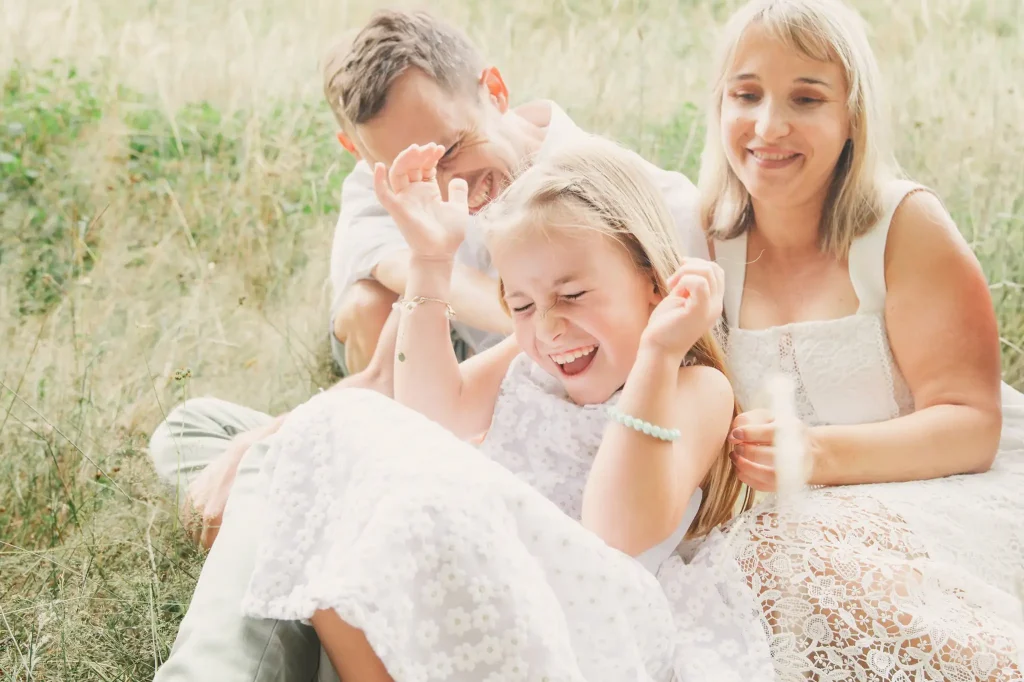Séance photo famille à Toulouse dans la forêt de Bouconne avec des parents qui chatouillent leurs filles pour la faire sourire.