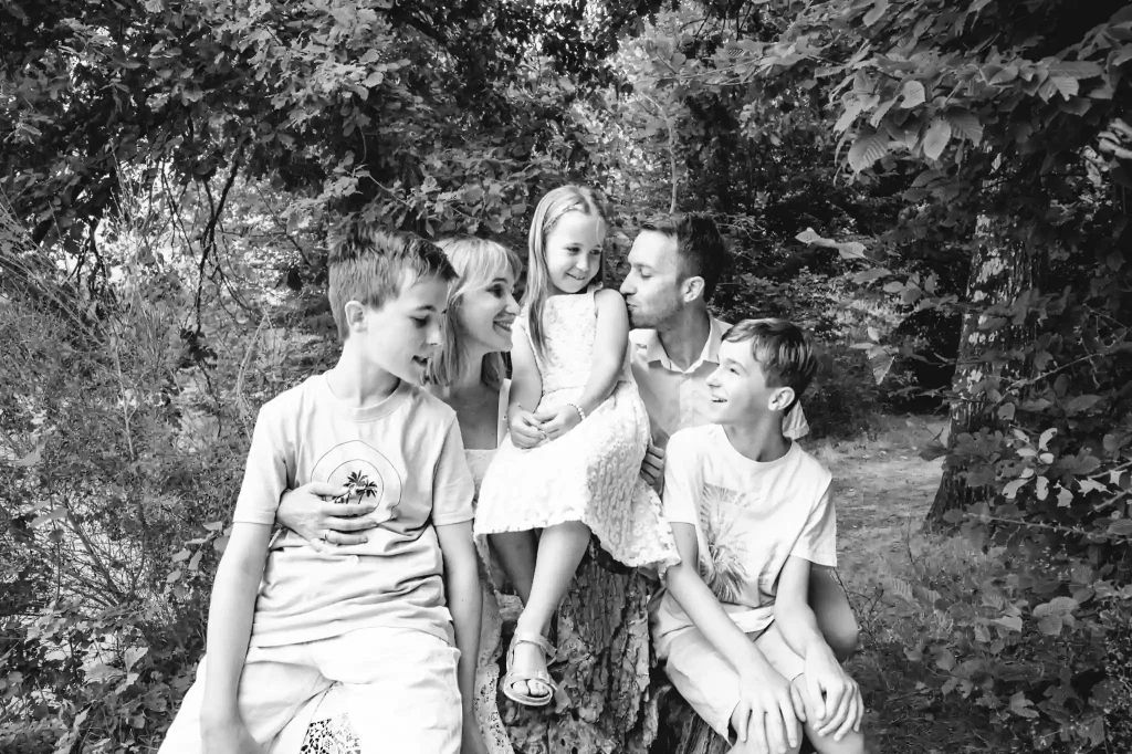 Séance photo famille à Toulouse dans la forêt de Bouconne avec une photo de famille sur une vielle souche d'arbre.