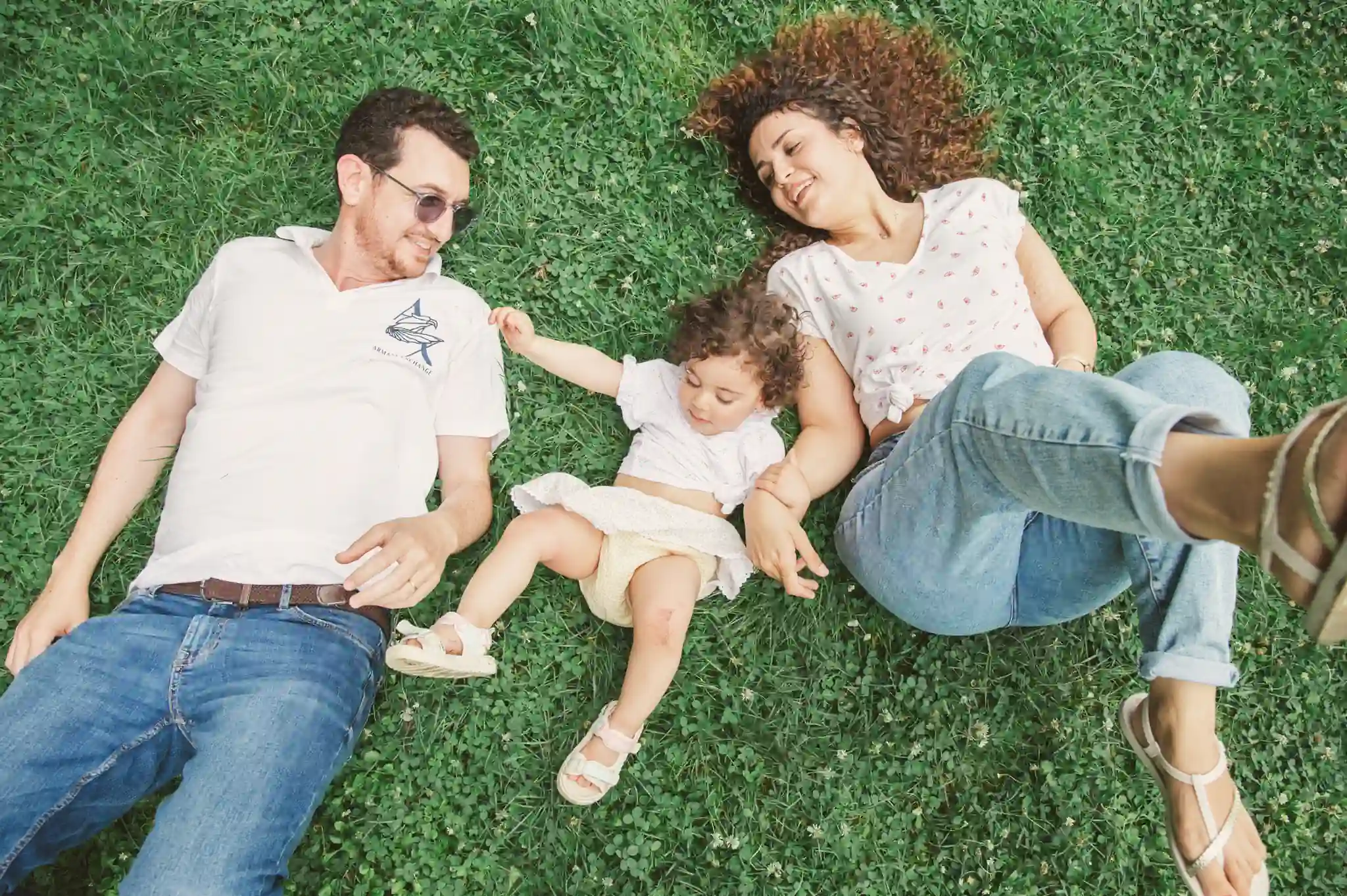 Séance photo famille à Toulouse au jardin des plantes avec les parents qui se roule dans l'herbe en riant aux éclats avec leur fille