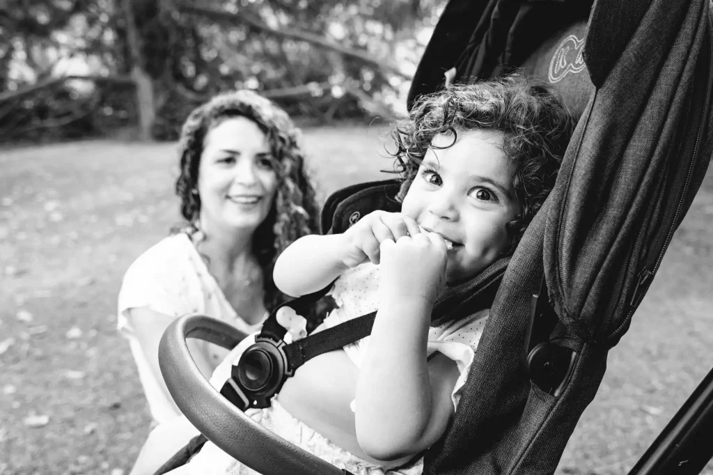 Séance photo famille à Toulouse au jardin des plantes. La maman regarde sa fille heureuse de manger un gâteau dans sa poussette