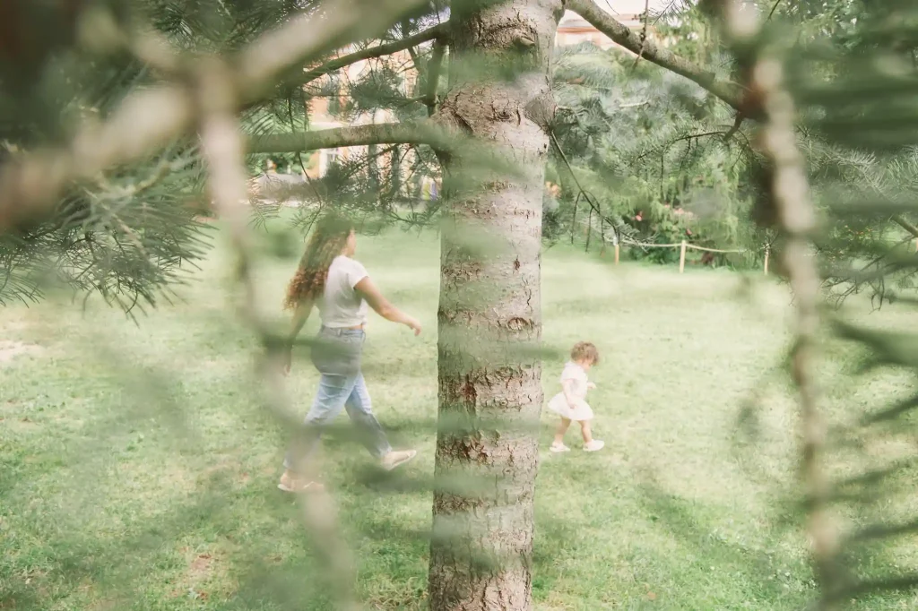 Séance photo famille à Toulouse, au jardin des plantes, avec la maman qui court derrière sa fille qui joue entre les arbres