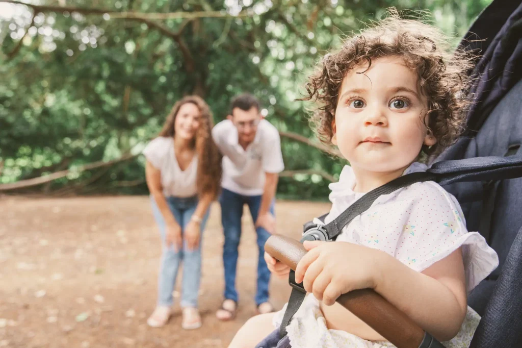 Séance photo famille à Toulouse au jardin des plantes. Les parents appellent leur fille assise dans la poussette