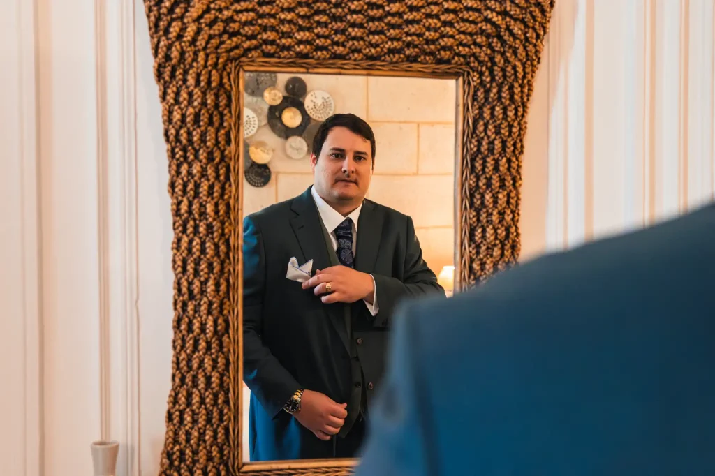 Le marié ajuste sa pochette devant le miroir à la fin des préparatifs avant d'aller se placer pour la séance first look.