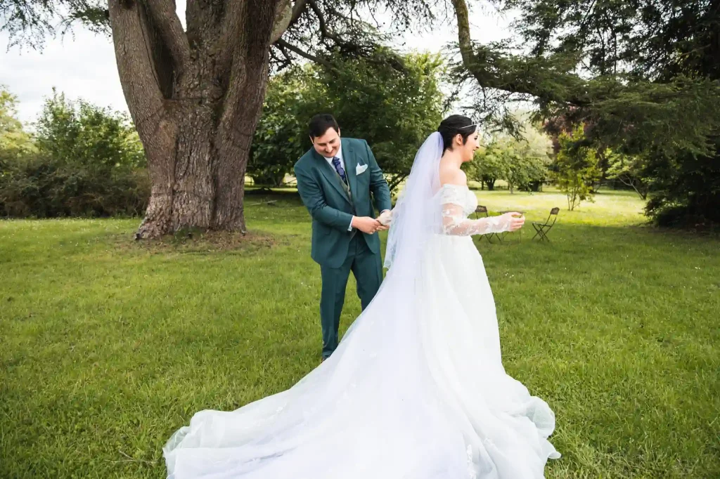 Le marié découvre la robe de mariage de sa femme lors de la séance du first look avec leur photographe de mariage.