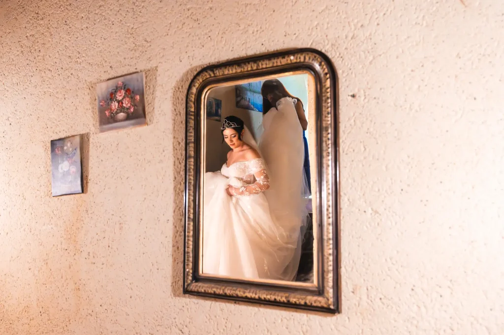 La mariée descend les escaliers à l'aide de sa témoin qui lui tien la traîne afin de retrouver son mari pour la séance photo du first look.