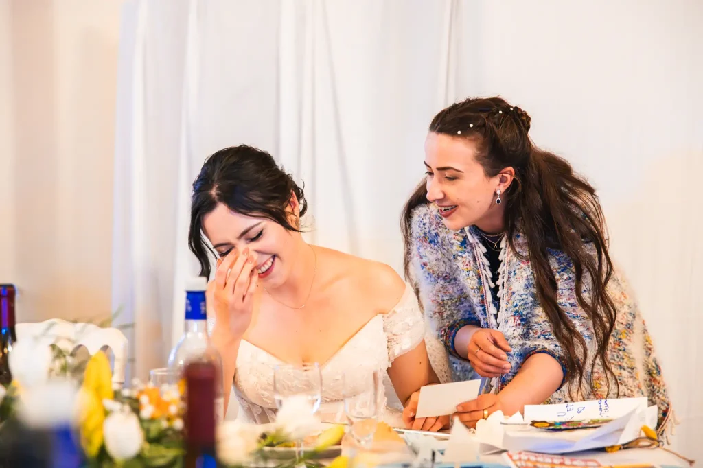 La mariée rit aux éclat en découvrant le cadeau de sa sœur pendant le repas du mariage
