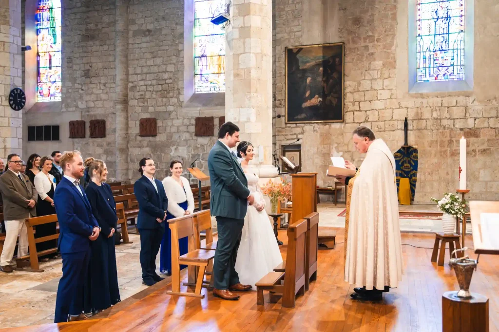 Les mariés reçoivent les bénédictions du prêtre devant leurs témoins souriants.