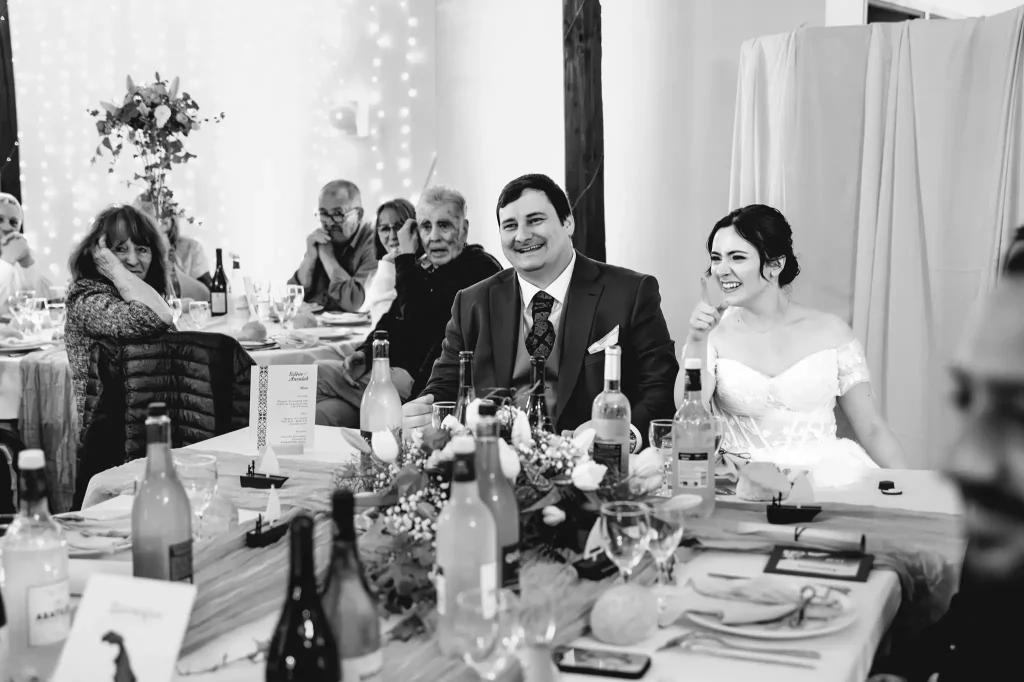A leur table, les mariés rient aux éclats prenant un sketch des parents du marié.