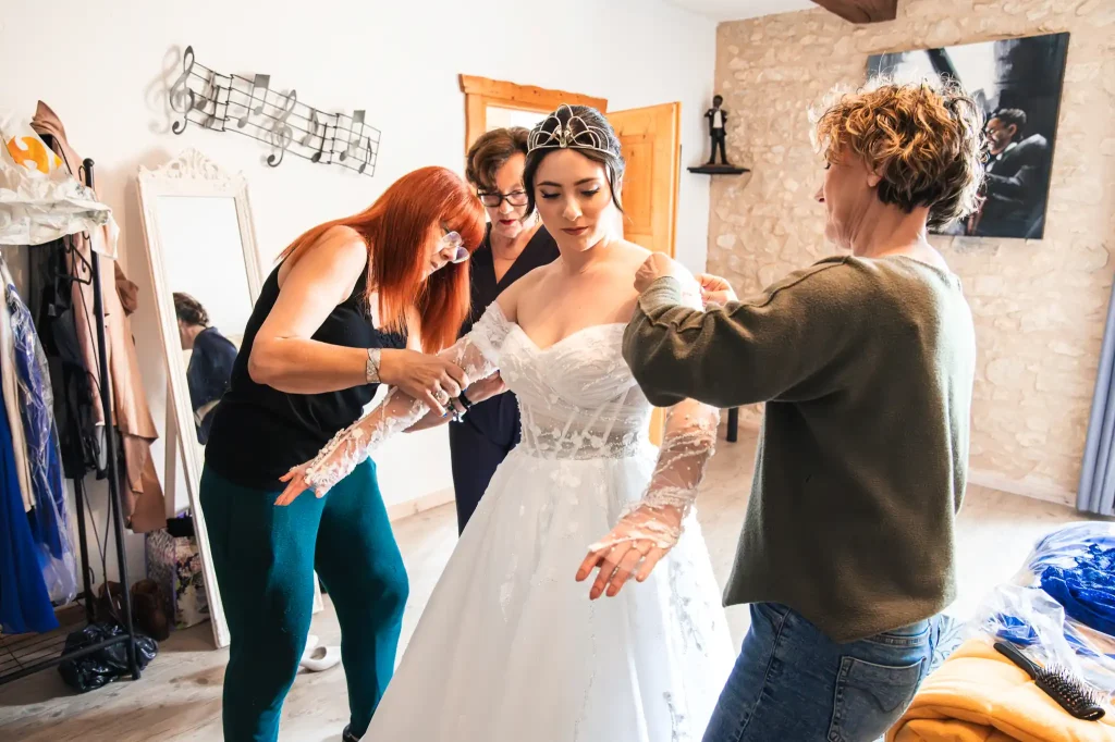 La mère et la belle-mère aide leur fille à s'habiller et à enfiler sa robe de mariée de chez Robe Elysée à Toulouse